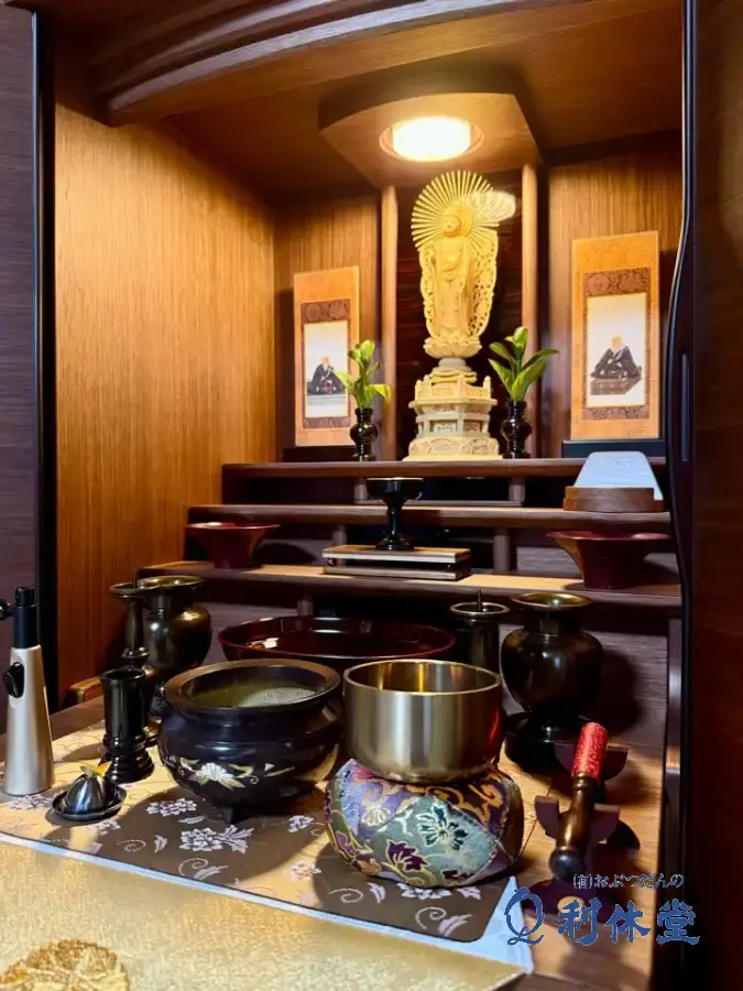 幅広モダン仏壇の内部をクローズアップ。天井のLEDライトに照らされた柘植の阿弥陀如来立像と、澄んだ音色の佐波理りん「勘三郎りん」、御室型京仏具の花立などが鮮明に見える、浄土真宗本願寺派の荘厳。