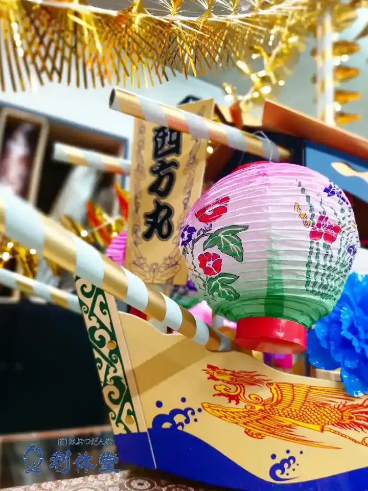 長崎市仏壇・仏具店「おぶつだんの利休堂」2026年版の店頭展示精霊船。西方丸の札やほうずき提灯、モールで装飾された板紙船キットのアップ。