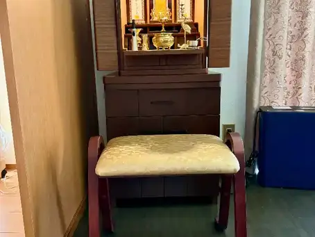 長崎の仏壇・仏具店「おぶつだんの利休堂」が時津町久留里郷のお客様宅へ、ウォールナット材のモダン仏壇を専用下台と椅子とともにリビングに配置した様子。