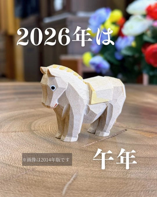 (全体のショット): 長崎の仏壇店のおぶつだんの利休堂の店内で撮影された、2014年版の大仏師・松本明慶工房謹製「干支 午の木彫りの置物」の全体像。一刀彫特有の力強い角ばった雰囲気ながら、馬の目、口元、たてがみ、鞍(くら)には金色の着色が施され、風格と華やかさを添えています。背景には仏壇店の落ち着いた空間が広がっています。 ※画像は2014年版です。