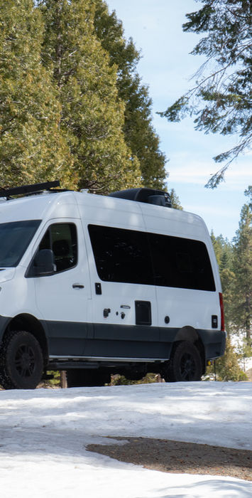 White camper van on a snow-dusted road among trees