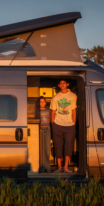 Two people standing in an open camper van door at sunset
