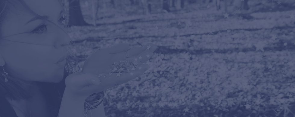 Photograph of Ceryn Rowntree, a dark haired white woman, standing in a forest blowing silver stars from her hands as she looks to the right of the screen. Photo is covered in a blue tint and is by Laura Pearman photography.
