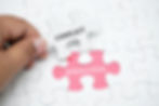 Picture of a white puzzle a hand reaching into the frame is picking up one piece which says 'CONFLICT' revealing a pink piece that says 'RESOLUTION'.