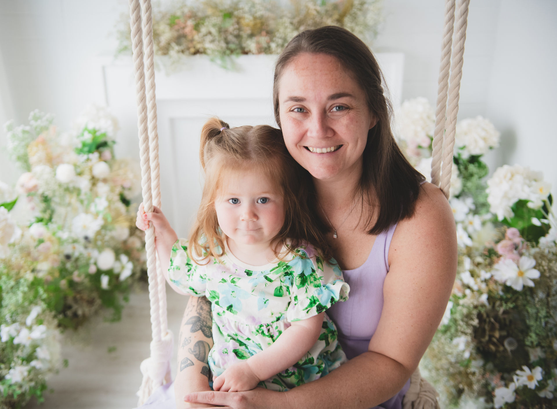 mom and toddler girl on a swing surrounded by flowers