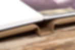 Close-up of an open photo book on a tan stand atop a wooden table, showing white page edges and a soft, neutral scene