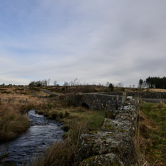 Stone bridge crosses flowing stream on a cloudy day, Thorn Valley Studios.