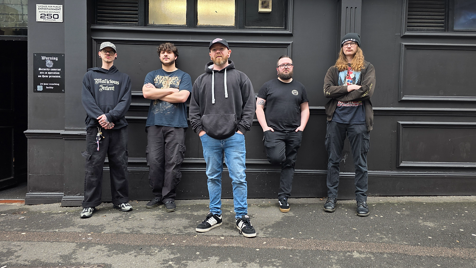 Five men in dark casual clothes pose against a black wall outside a venue with security and occupancy signs.