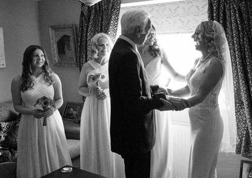 Bride and father holding hands WEDDING PHOTOGRAPHY in front of bridesmaids and window.