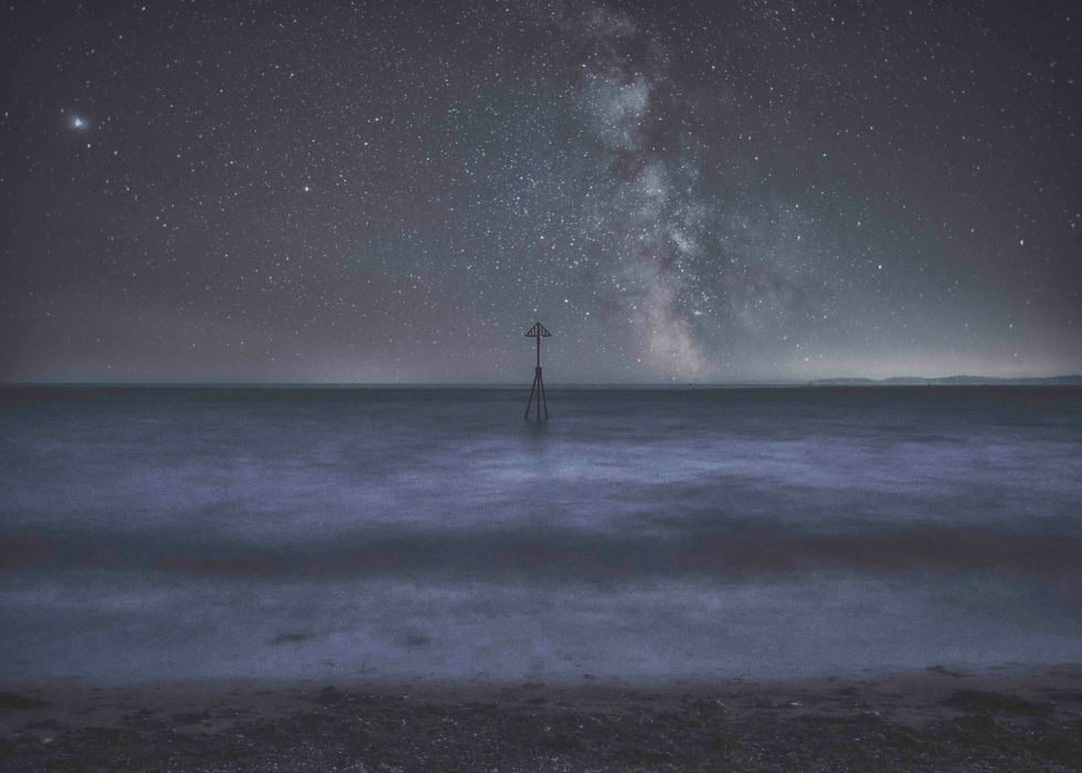Milky Way over a calm dark sea, with a lone navigation marker silhouetted in the center under a star-filled night sky.