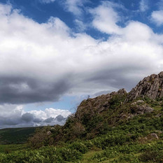 Rocky outcrop with green vegetation under cloudy blue sky, landscape view.