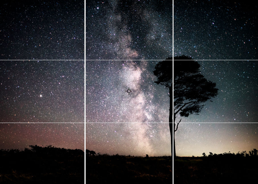 Milky Way glows over a star-filled night sky, with a lone tree silhouette above a dark landscape.