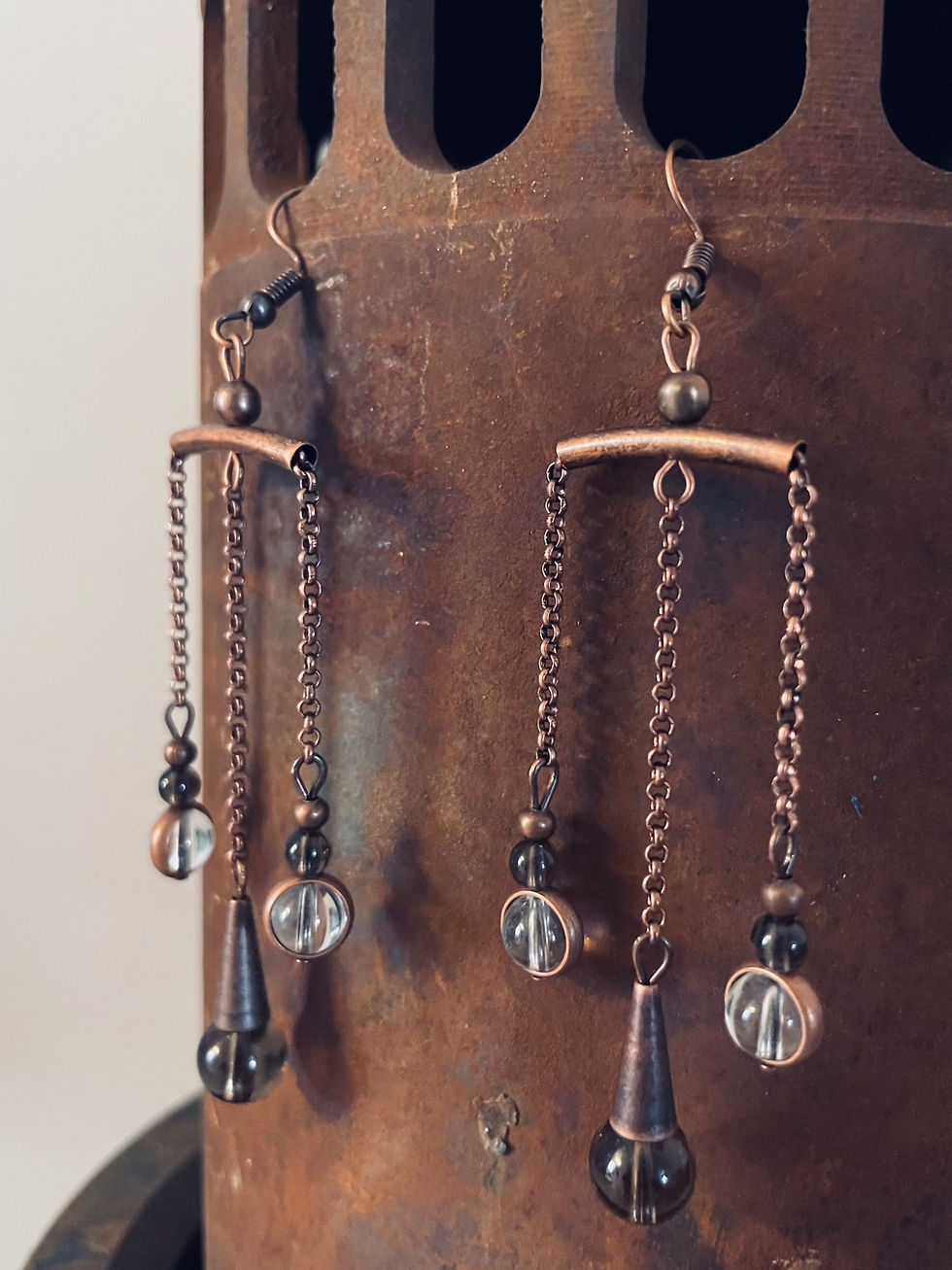 Thumbnail: Copper with clear and smoky quartz earrings dangle from a rusted pipe