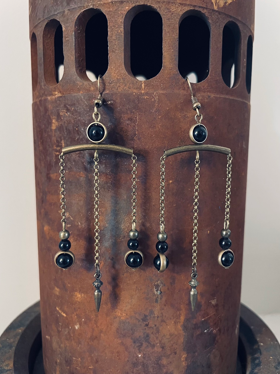 Brass and onyx bead earrings dangle from a rusty metal pipe