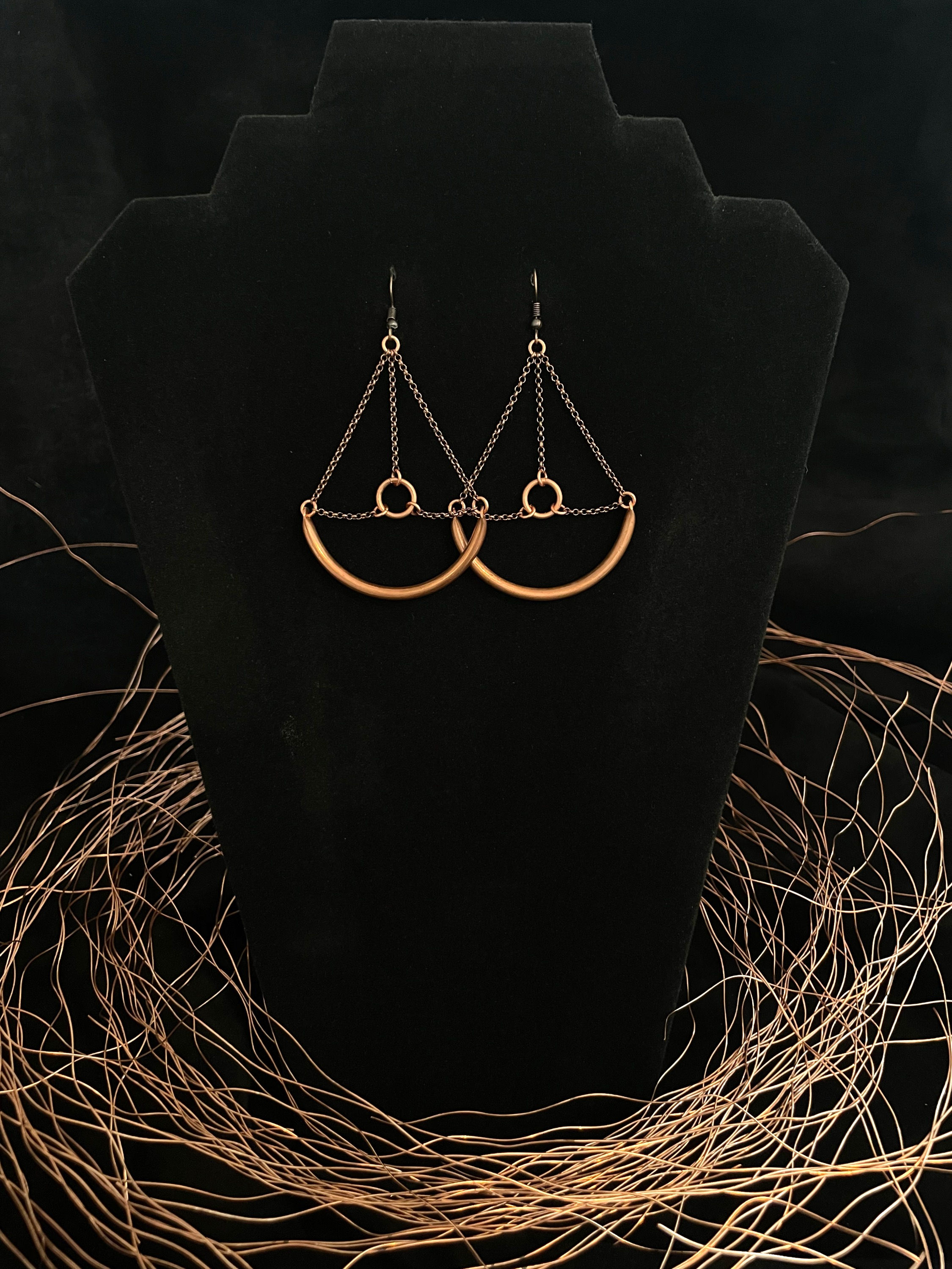 Hollow copper piping and copper chain earrings dangle on a black velvet background