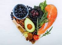 A heart-shaped arrangement of healthy foods: salmon, avocado, blueberries, nuts, and greens on a white background, conveying health and wellness.