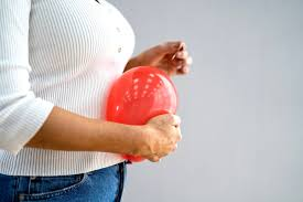 Person in white sweater and jeans holds a red balloon against a plain gray background. The mood appears calm.