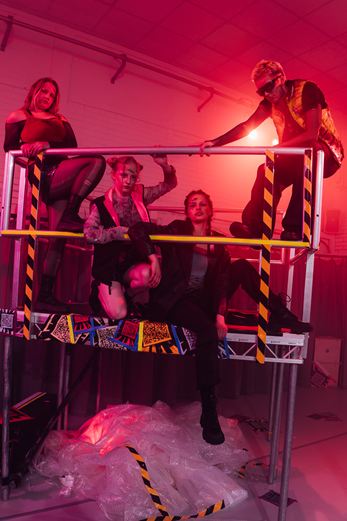 Photo of dancers on a raised platform. The lighting is red.