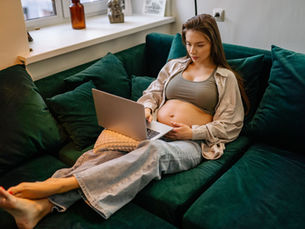 Femme enceinte installée sur un canapé avec son ordinateur portable