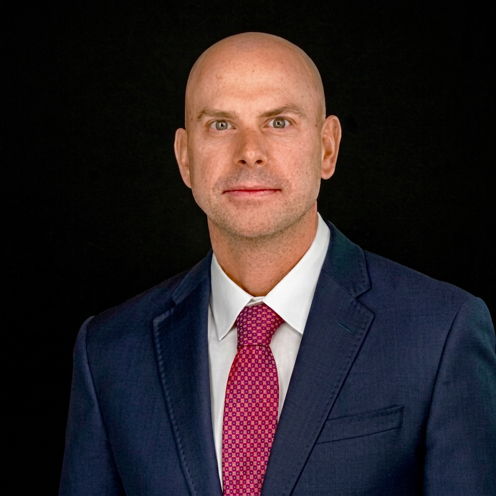 Portrait headshot of Dan Cuneo in a dark suit and red tie