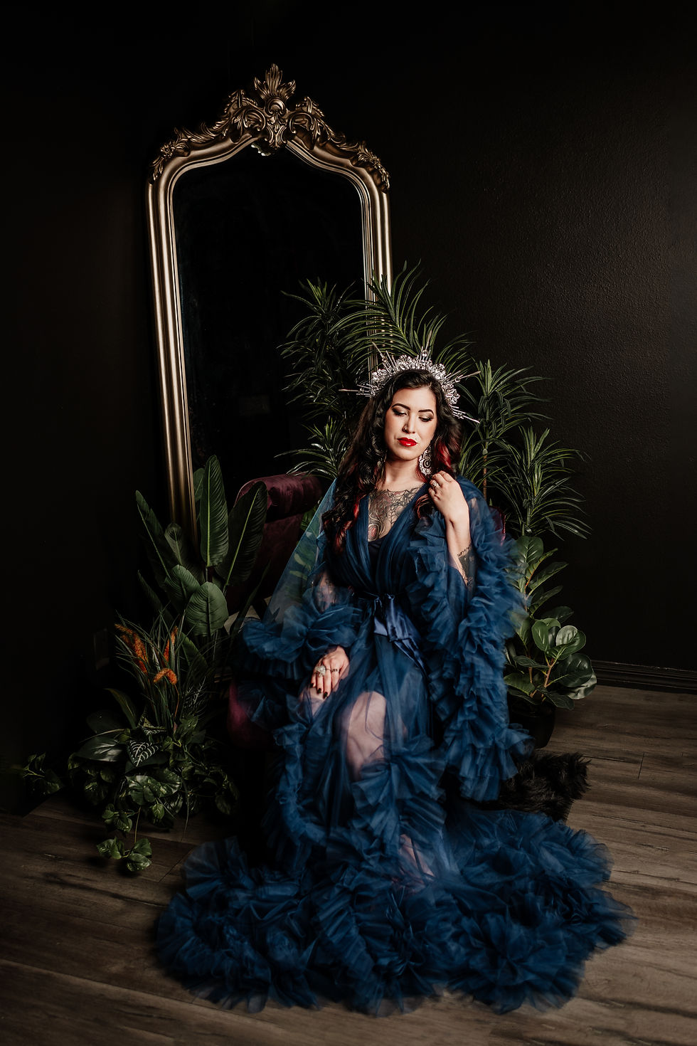 Dark feminine portrait of a woman with black hair, tattoos, and a sheer navy blue ruffled gown during a goth glam photo session in Orlando.