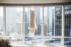 A stunning wedding dress hung against a floor to ceiling window overlooking a river and urban enviro