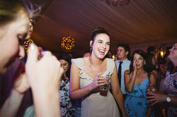 A happy wedding guests dances while holding her cocktail on the dance floor.