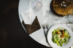 A detailed photo of a table setting at a wedding lunch with a menu, salad, and candle.