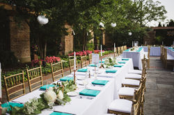 An outdoor wedding dinner setting with long tables with gold chairs, tall candles, blue napkins, and