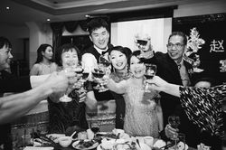A group of joyous wedding attendees share in a Chinese wedding tradition by gathering around the tab