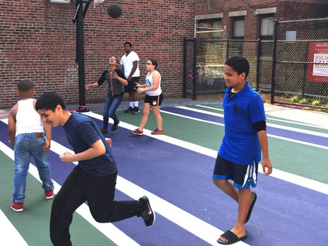 teens playing basketball on a green and purple striped court between buildings.