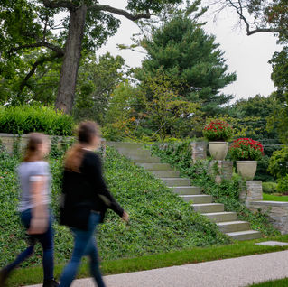 two people walking past a planted embankment with steps leading up.