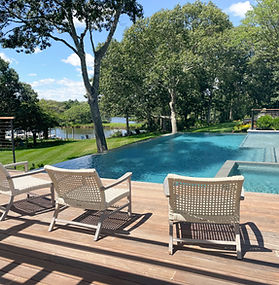 Infinity edge pool and with pool chairs overlooking lawn to a lake