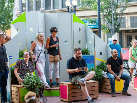 a group of people gathered in the parklet sitting on brightly painted benches.