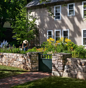 Stone wall with flower garden and gardener beyond.