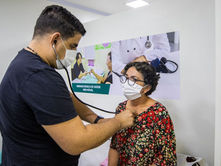 Médico, em unidade hospitalar, ausculta paciente feminina.