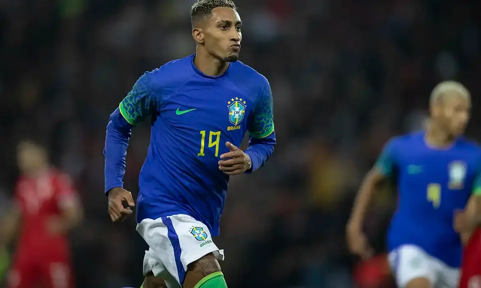 Jogador Raphinha, da seleção brasileira, correndo em campo em uniforme azul e branco.
