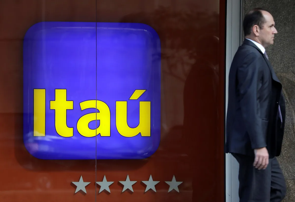 Homem de terno passando em frente a faixada com logo do banco Itaú.