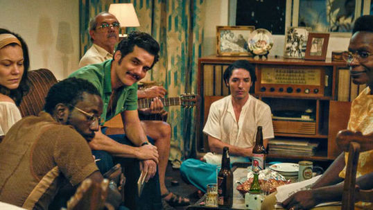 Cena do filme O Agente Secreto, com Wagner Moura e atores em sala e cervejas na mesa.