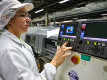 Mulher com vestes da indústria mexe em maquinário de fábrica.