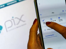 Tela com logo do Pix e celular com mão em botão de pagamento.