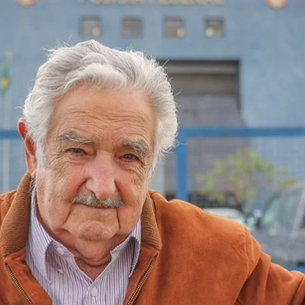 Foto de Pepe Mujica, ex-presidente do Uruguai, com uma blusa laranja erguendo o punho em saudação.