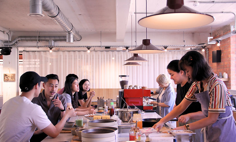 group of female workers behind coffee and kitchen bar and customers seated in front of them dining