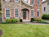 Two-story house with brick, stone, red shutters, and lawn.