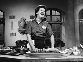 Julia Child cooking in a kitchen laughing