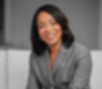 Smiling woman in gray suit sitting on a sofa, business portrait of Dr. Angel Jones.