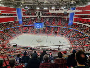 A packed arena viewed from high in the stands during an NHL Global Series game, red and blue seating filling the bowl around the ice.
