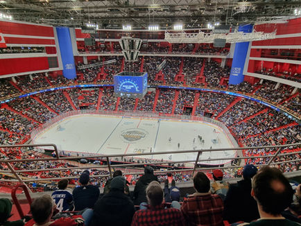 A packed arena viewed from high in the stands during an NHL Global Series game, red and blue seating filling the bowl around the ice.