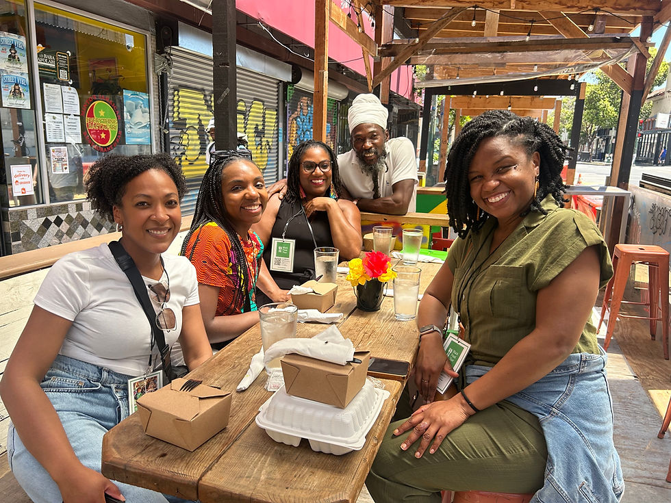 A joyful group of guests enjoys a sunny stop on a Black food tour in Oakland, sharing smiles and culture over a meal.