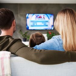 Family sitting on couch in living room watching TV.